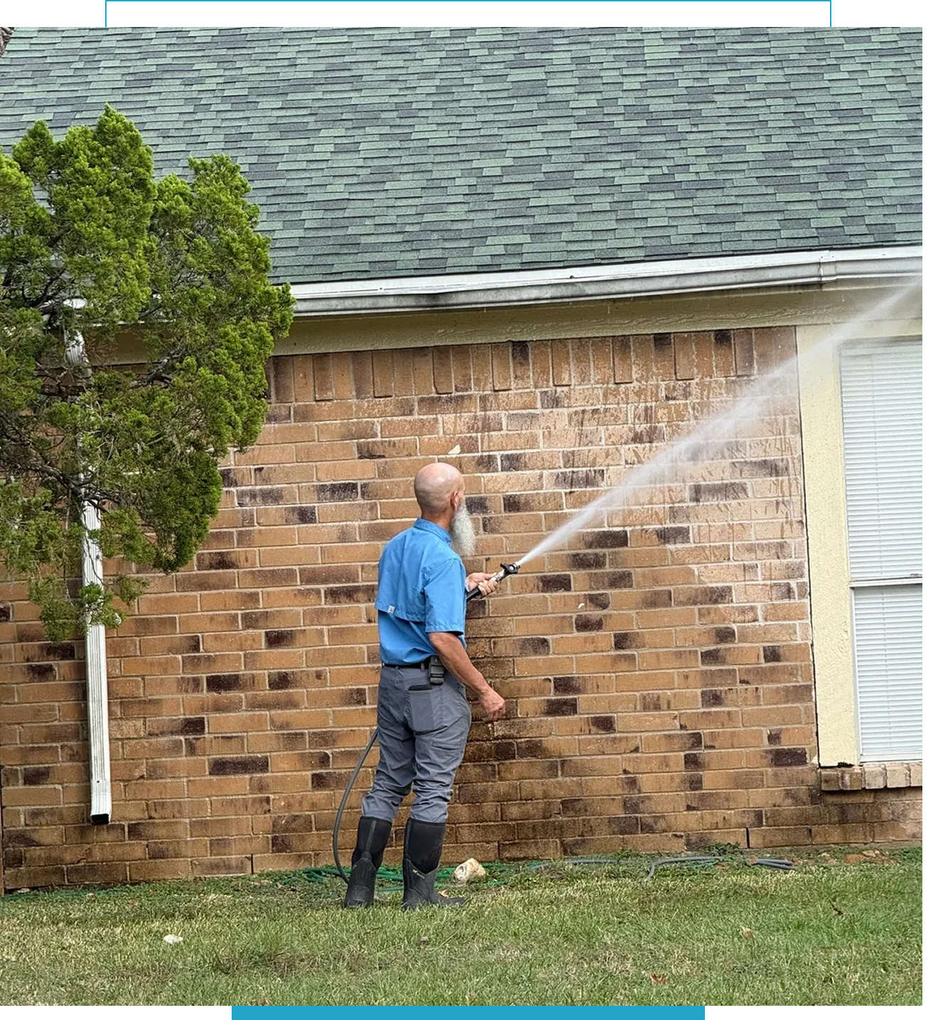 Man spraying water on a brick house exterior with a hose.